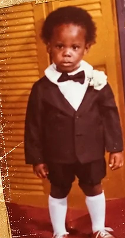 Thomas as a little boy in a tuxedo and bow tie, standing in front of a wooden louvered door